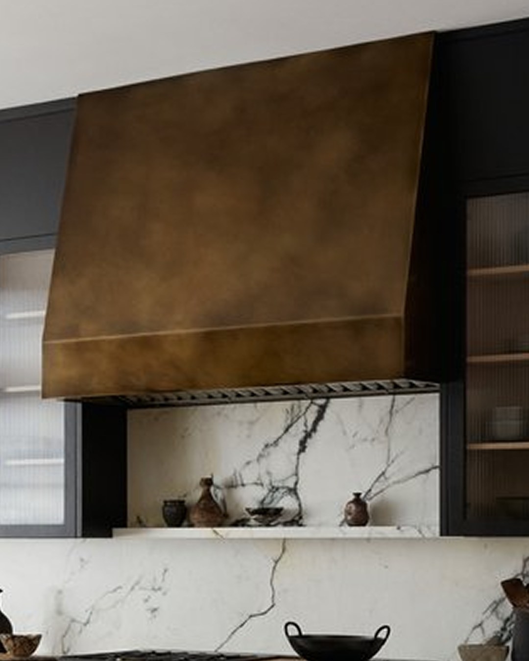 A finished Alli Made raked hood in aged brass above a marble backsplash and shelf